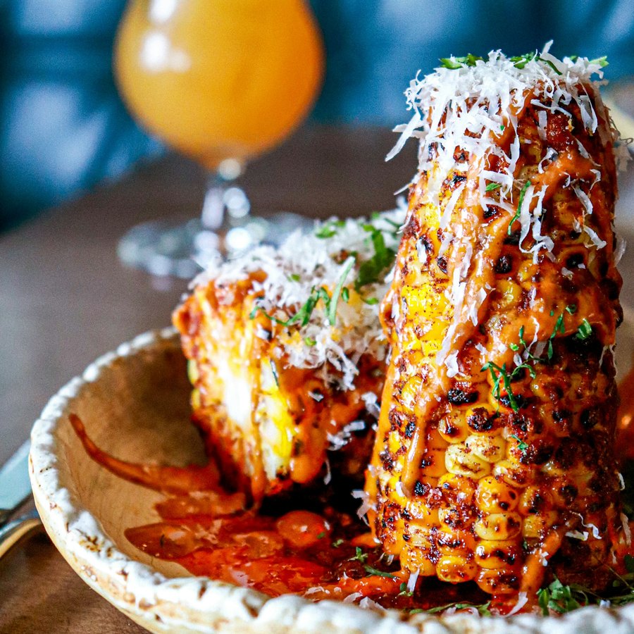 Grilled street corn with chile sauce, grated cheese, and herbs.