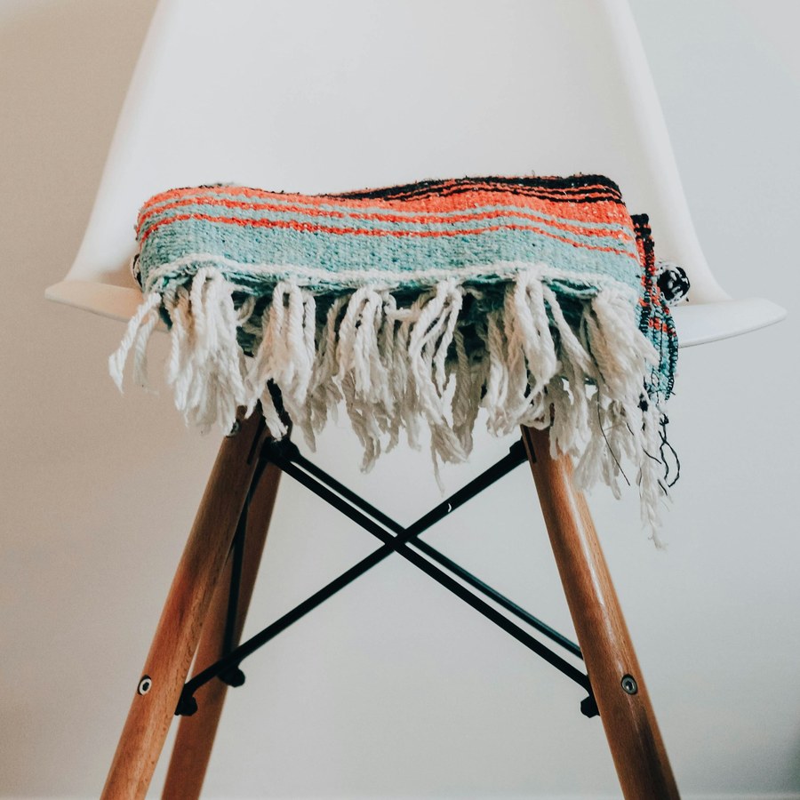 a teal and coral striped fringed textile draped over a white chair