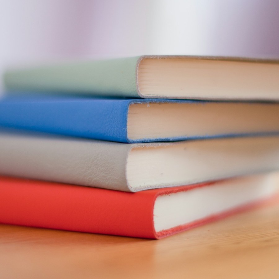 four stacked softcover notebooks in mint, blue, gray and red