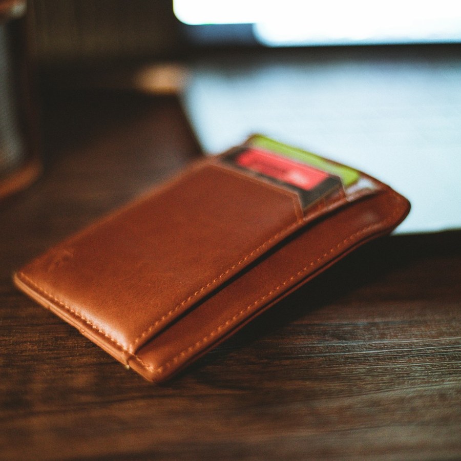 a cognac-brown leather card sleeve on a dark wooden tabletop
